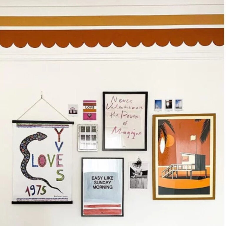 A wall with multiple hanging picture frames and a bold border painted on the top half of the wall.