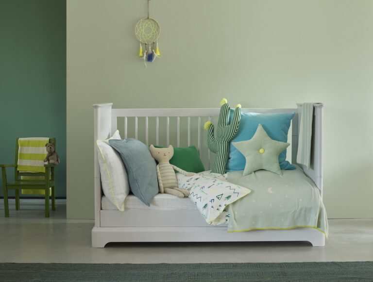 A cot in a nursey in calming green shades.