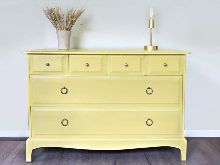 A beautifully painted yellow drawer set with simple decorations against a white wall.