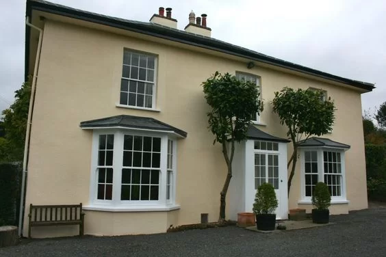 Exterior of a house with double bay windows and two small trees on either side of the front door.