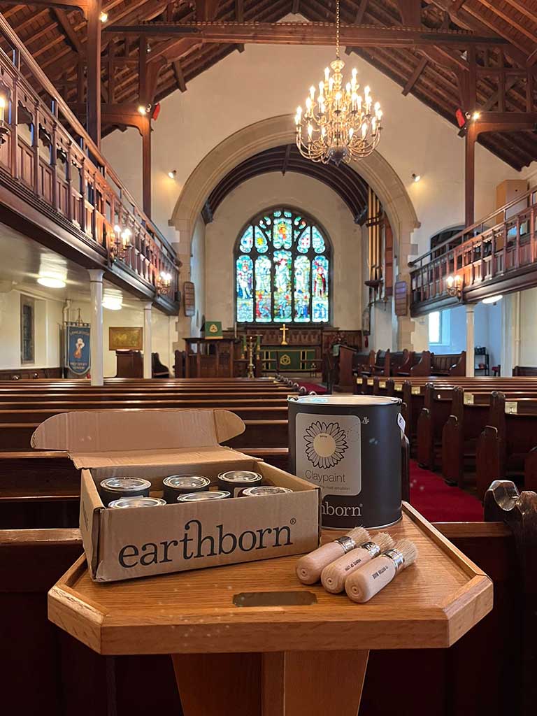 Earthborn paint tins and brushes on on a wooden table inside an old Church.