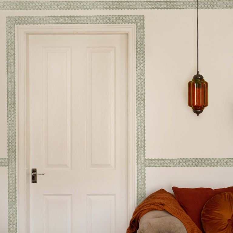 A white wall with a patterned green trim around the boarders and door frame.