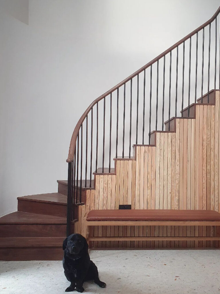 A carefully crafted wooden stair case with a cute little black dog at the bottom of the stairs.