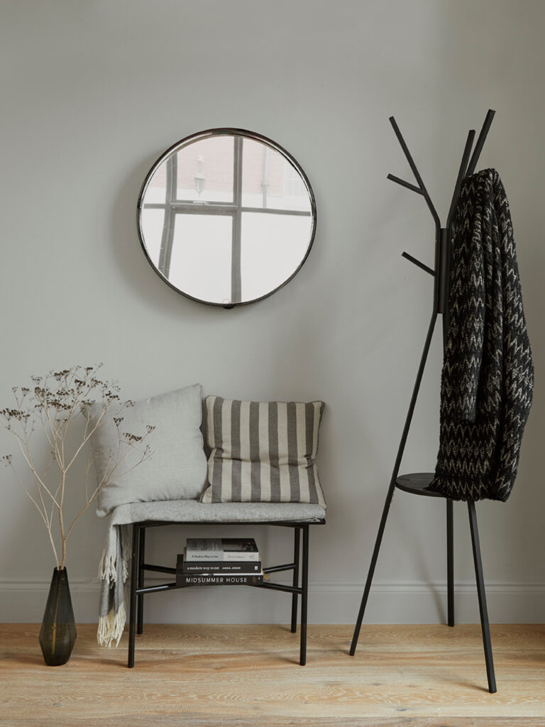 A seat below a circle mirror and a modern coat rack.