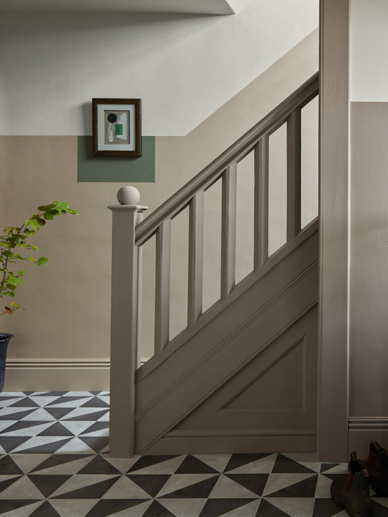 A patterned floor with a short banister leading upstairs. Colour blocking painted on the walls to add to the art hanging.