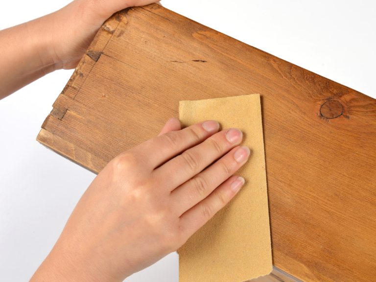 A close up of hands sanding a wooden draw in preparation.