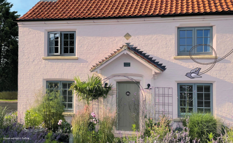 Painted brick house in a very pale pink with a garden and metal archway. Breathable Masonry Paint.