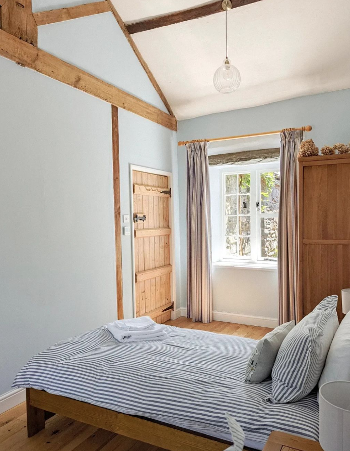 Pale blue bedroom with wooden beams and furniture.