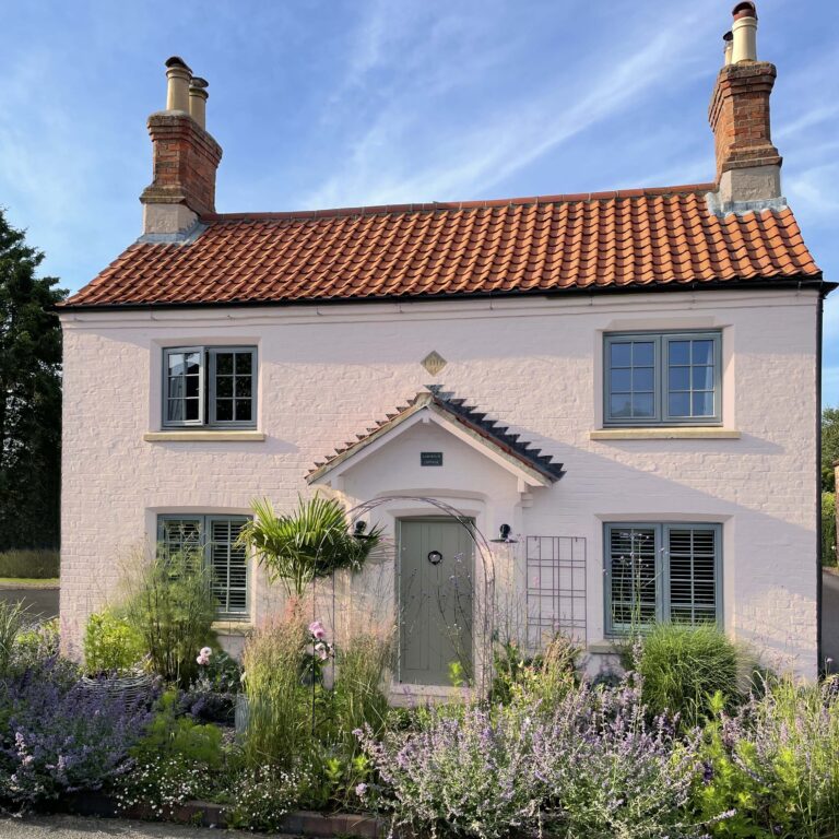 Old cottage with blue skies, a front garden and the road.