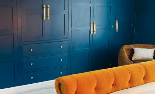 Deep blue wardrobe with a contrasting yellow bed and wooden beamed ceiling.