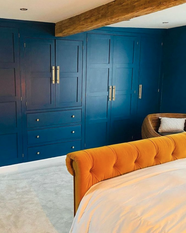 Deep blue wardrobe with a contrasting yellow bed and wooden beamed ceiling.