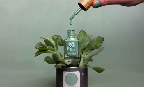 Green nail polish sitting in a plant that is potted in a small Earthborn paint tin.