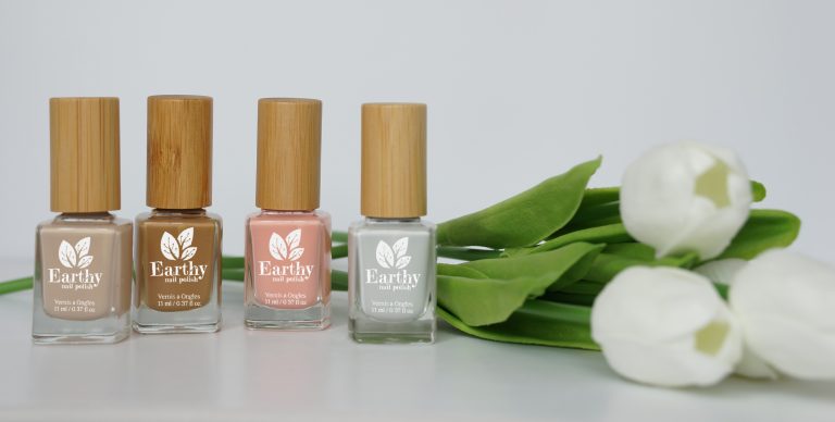 Earthy Nail Polish bottles in a row in front of white tulips.