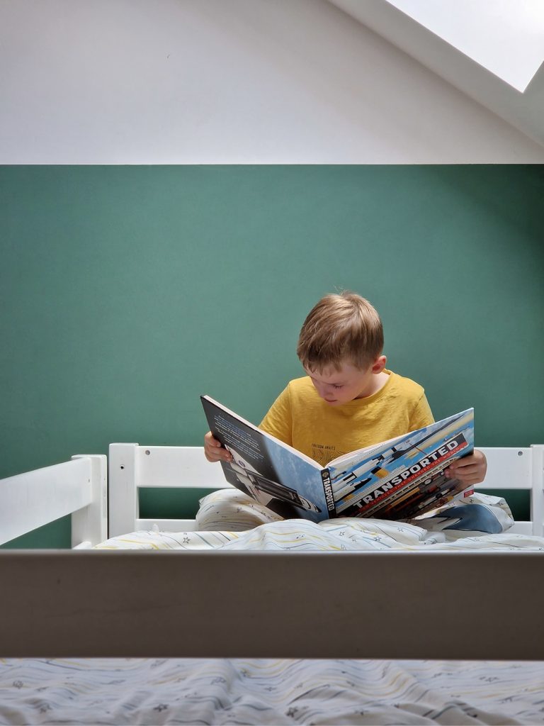 A child reading a book on a bunk bed.